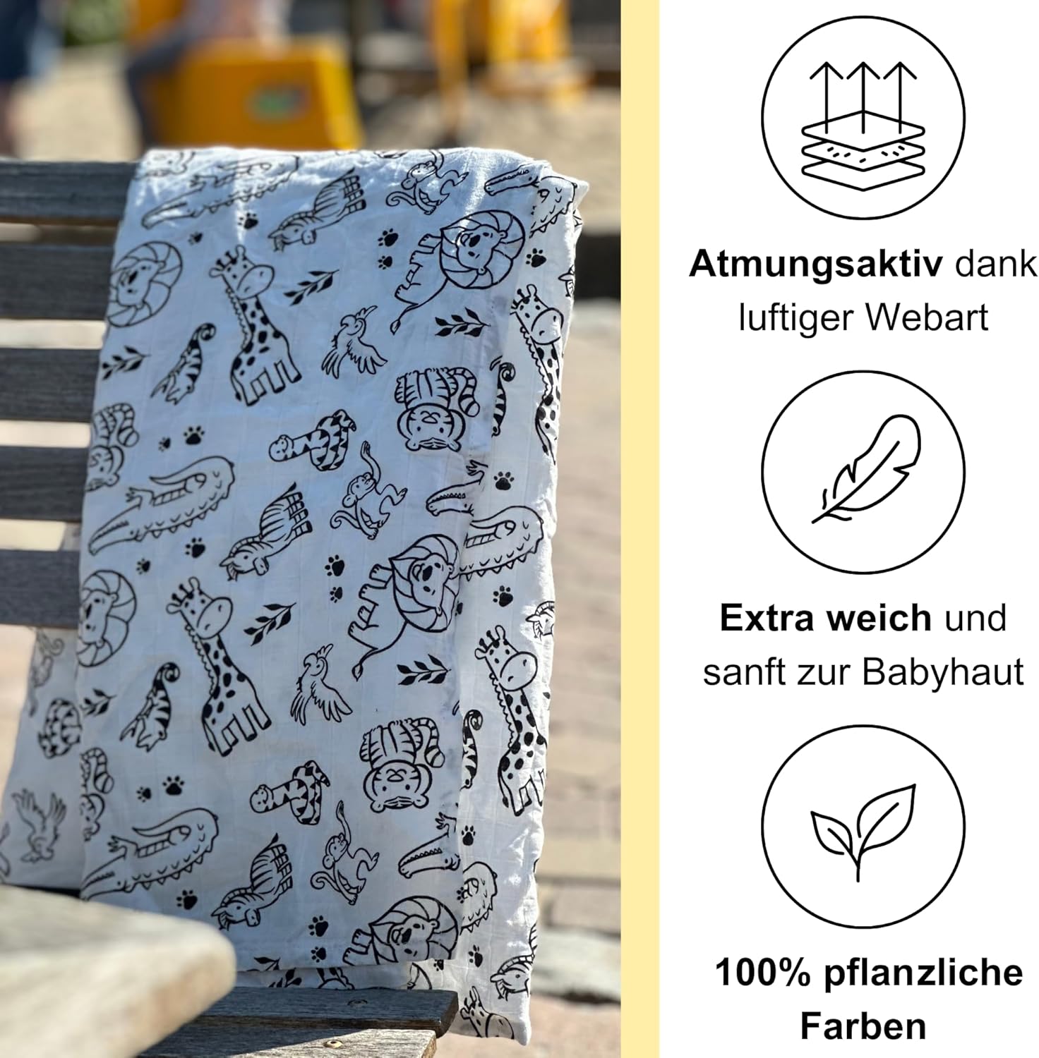 Kontrastreich bedrucktes Pucktuch mit schwarzen Tiermotiven hängt über der Lehne einer Parkbank im Sonnenlicht. Rechts daneben befinden sich drei Symbole mit Text: ‚Atmungsaktiv dank luftiger Webart‘, ‚Extra weich und sanft zur Babyhaut‘ und ‚100 % pflanzliche Farben‘.